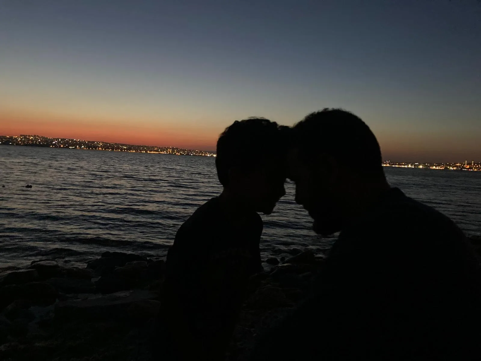 Silhouette of Mohammed Mansour and his son by the sea at sunset